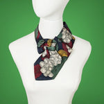 Load image into Gallery viewer, ascot scarf in muted fall colors of wine, gold, green and grey with a print of leaves and berries
